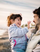 cute scene of dad holding and hugging her little daughter at the beach in winter